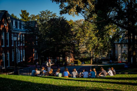 A class meets outdoors, during golden hour, on the Academic Quad on the Medford/Somerville campus.