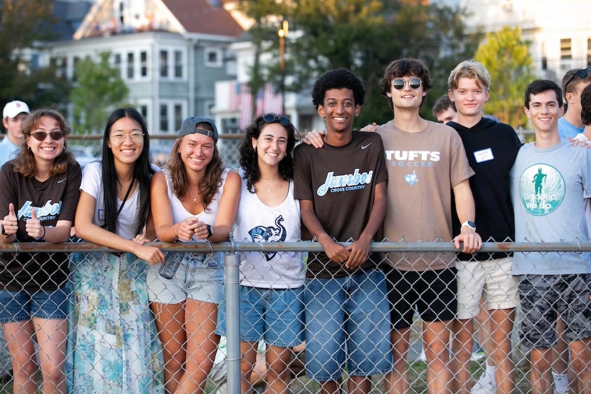 Eight students stand together smiling behind a fence